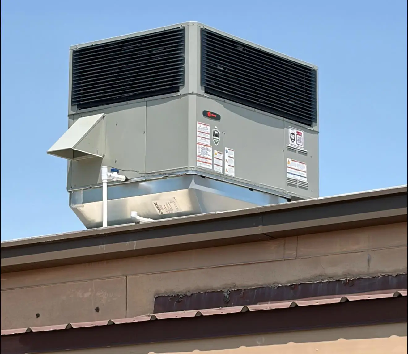 Commercial rooftop HVAC unit with large louvered vents mounted on a building roof against clear blue sky