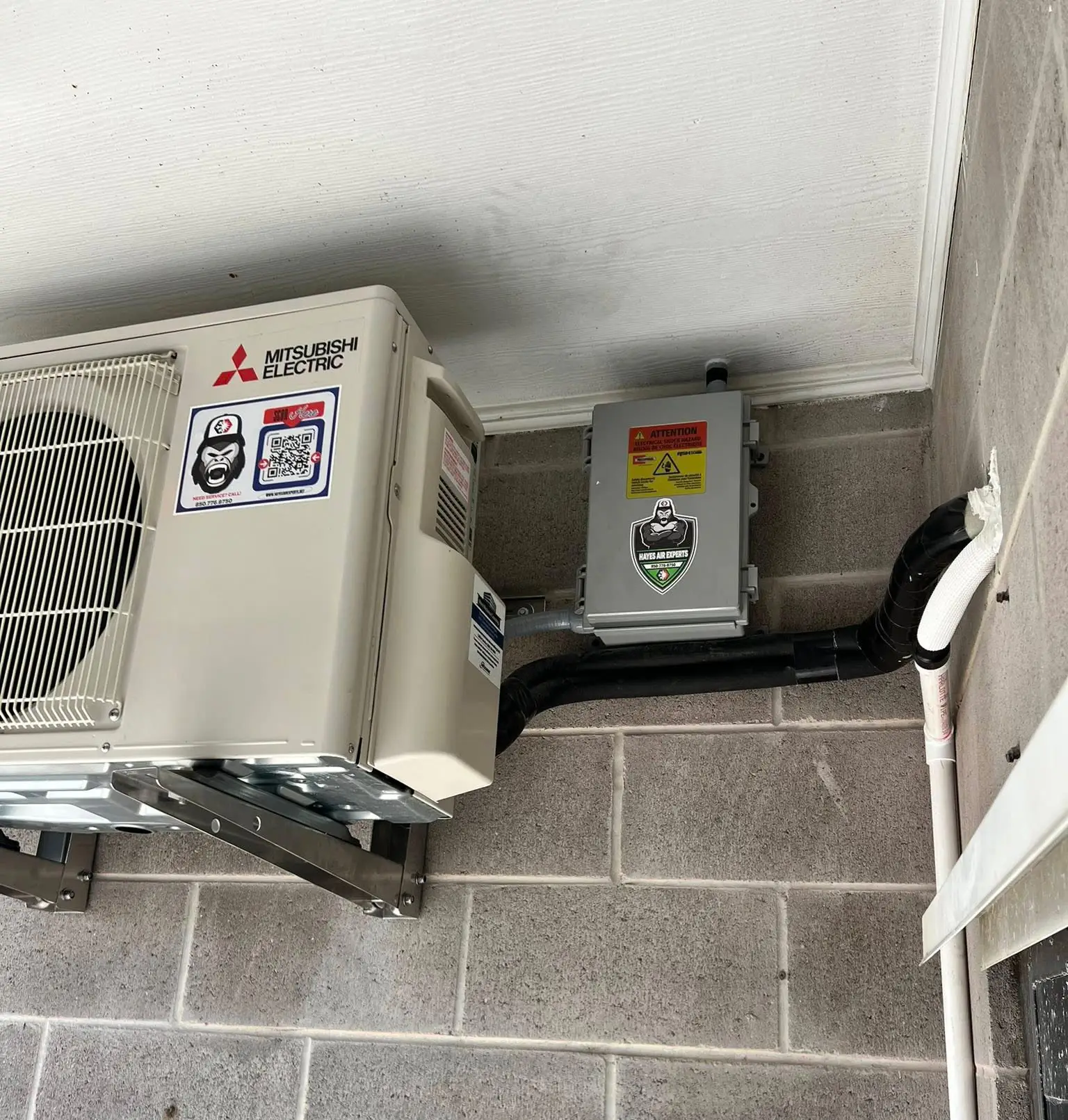 Mitsubishi Electric wall-mounted outdoor AC with disconnect box and insulated refrigerant lines on cinderblock wall