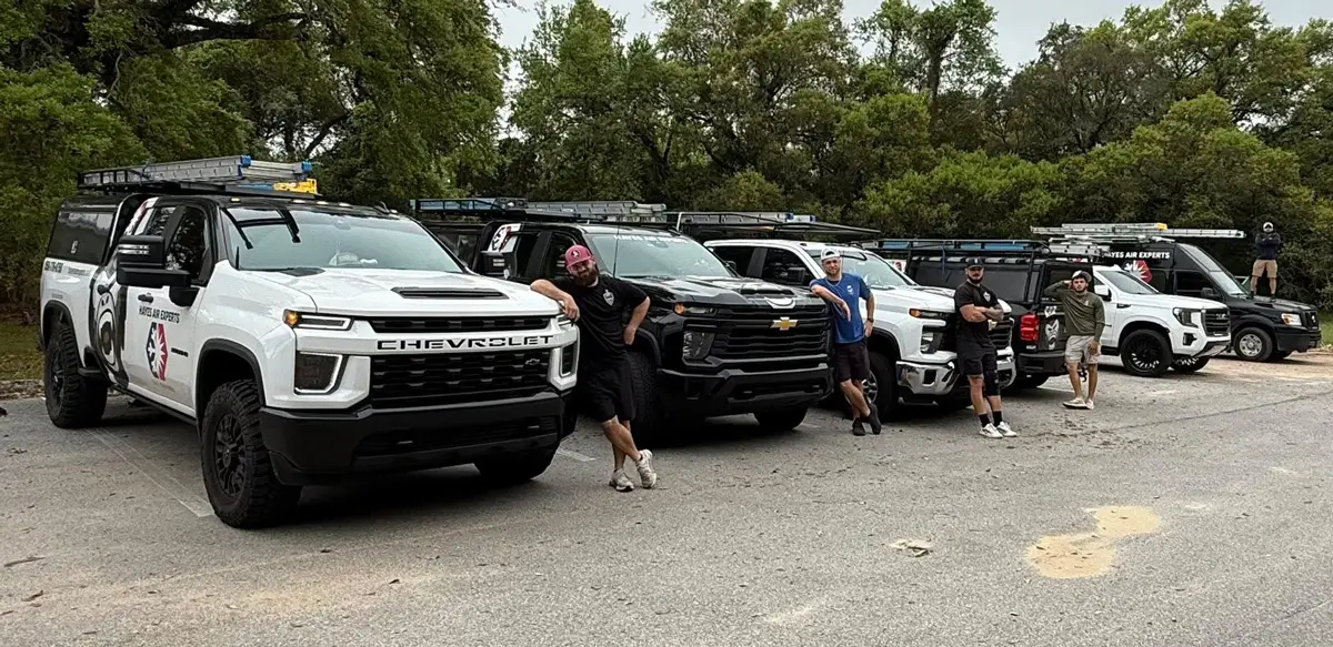 Group of men leaning on a row of branded Chevrolet service trucks parked in a wooded lot
