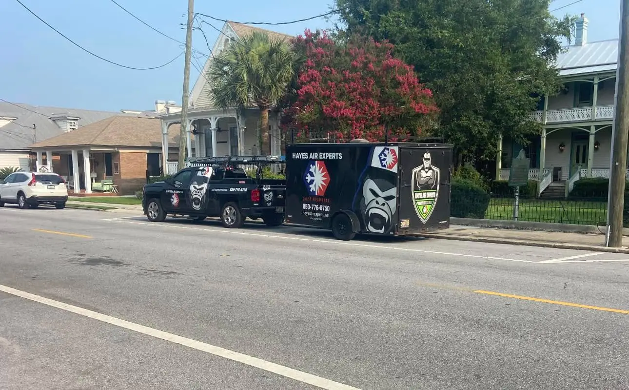 Black Hayes Air Experts truck and trailer parked on a residential street in front of Victorian houses and flowering trees