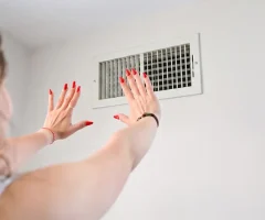 Woman with red nail polish reaching toward ceiling HVAC vent register