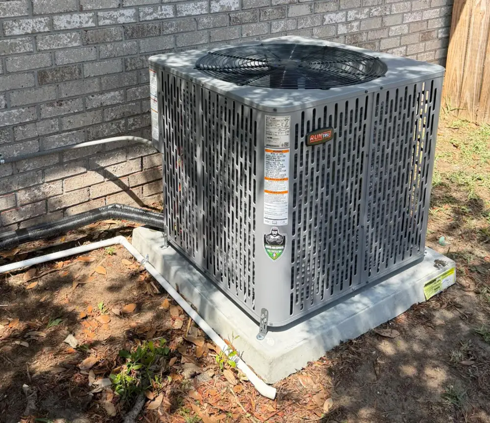 Outdoor gray HVAC air conditioning condenser unit on concrete pad next to brick house wall