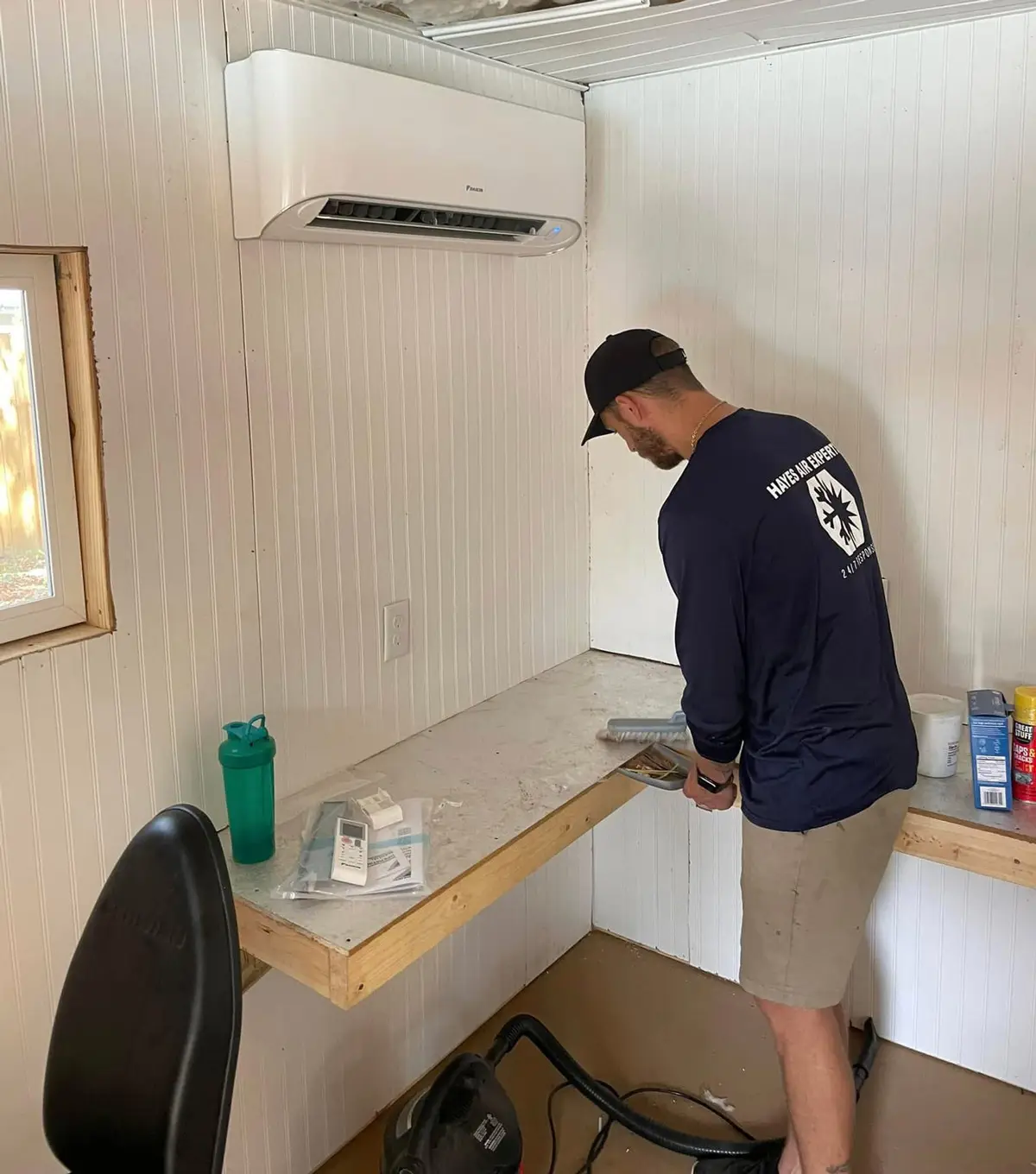 Man installing a ductless mini-split air conditioner in white-paneled room while working on a wall-mounted countertop