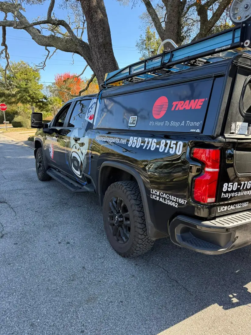 Black Trane service pickup truck with ladder rack and Hayes Air Experts graphics parked on a suburban street