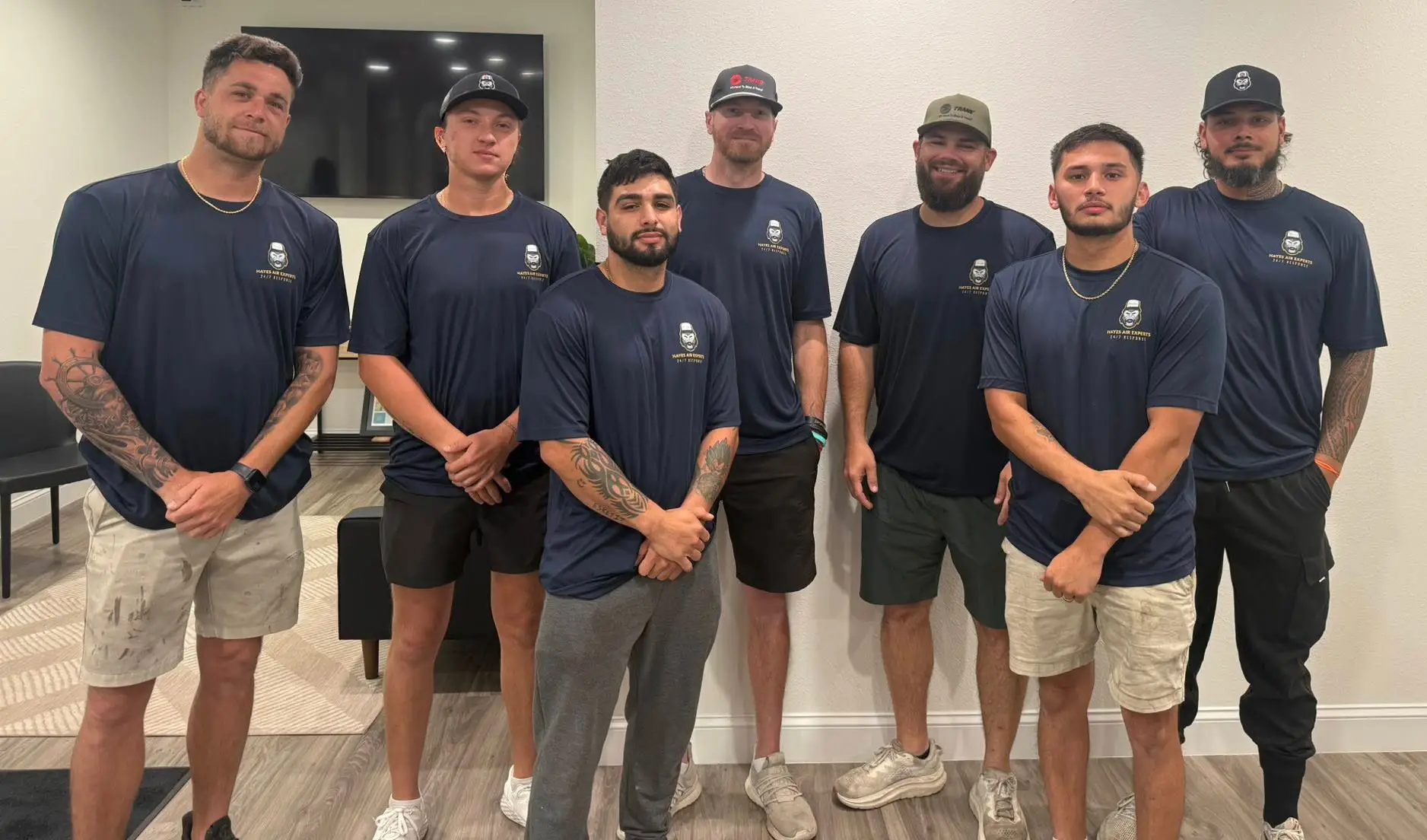Seven men in navy shirts with logo and caps standing in an office, posing for a group photo